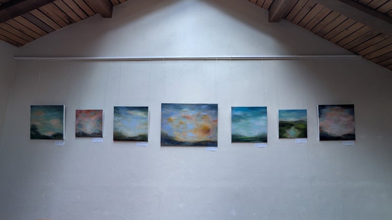 A line of oil paintings hang horizontal on a white wall